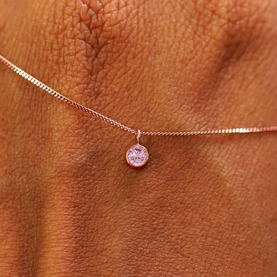 Close up view of a 14k rose gold Pink Sapphire Necklace draped across the back of a model's hand
