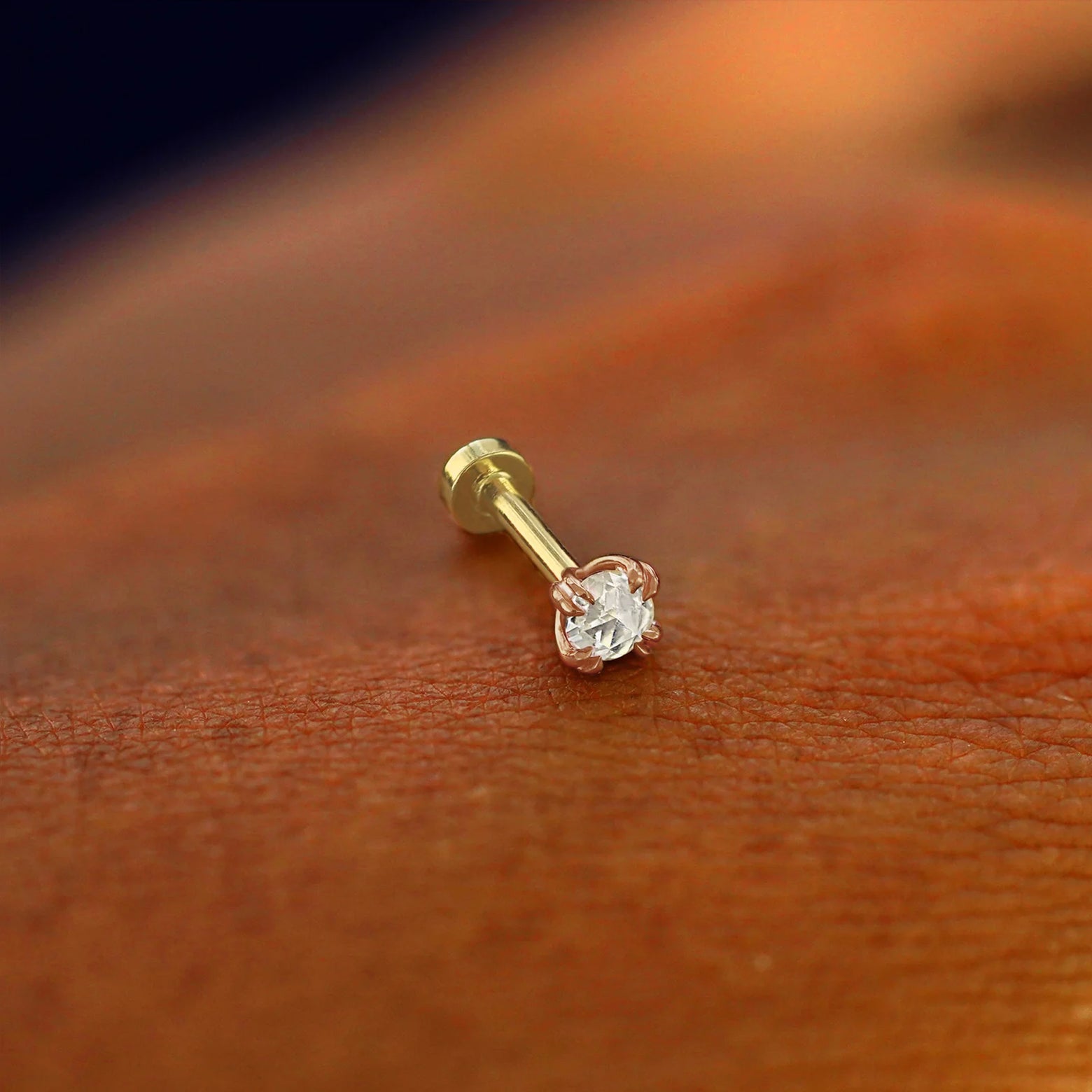 A solid 14k rose gold Rose Cut Diamond Flatback Piercing resting on the back of a model's hand
