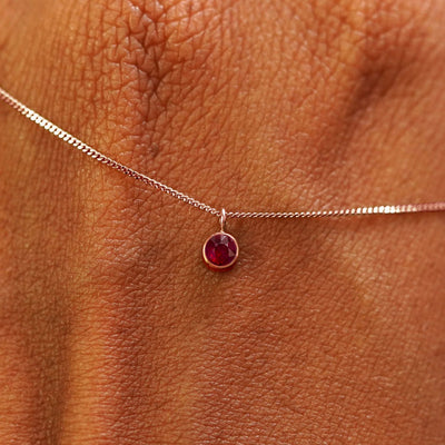 Close up view of a 14k rose gold Ruby Necklace draped across the back of a model's hand
