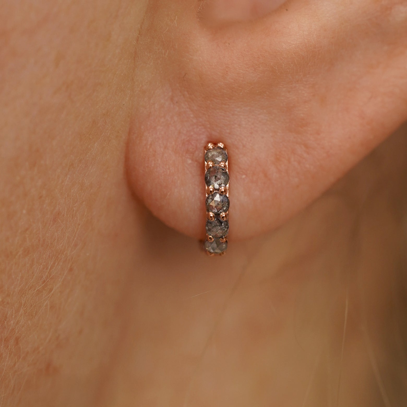 Close up view of a model's ear wearing a rose gold Mini Salt and Pepper Diamond Huggie Hoop