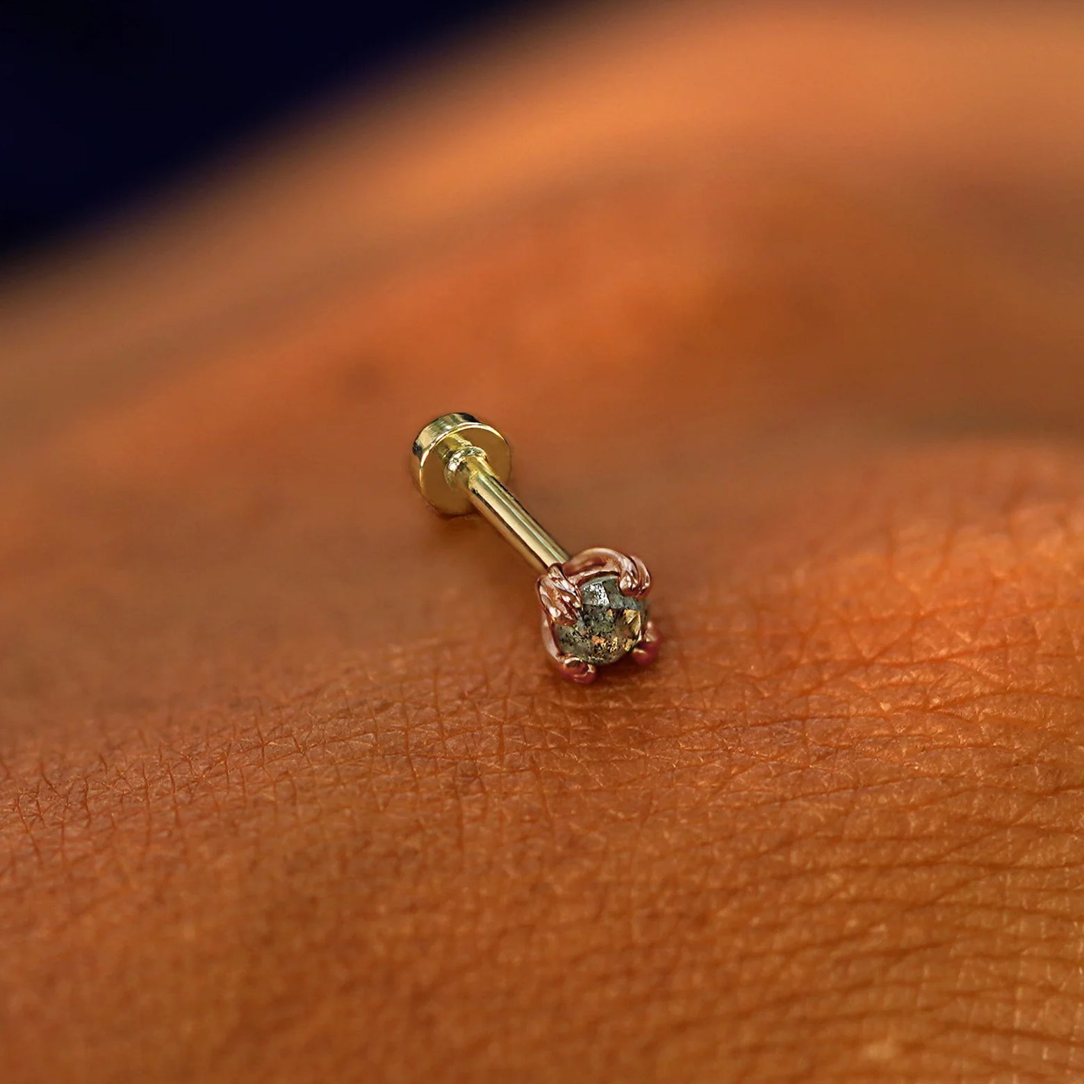 A solid 14k rose gold Salt and Pepper Diamond Flatback Piercing resting on the back of a model's hand