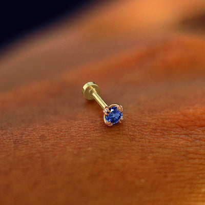 A solid 14k rose gold Sapphire Flatback Piercing resting on the back of a model's hand