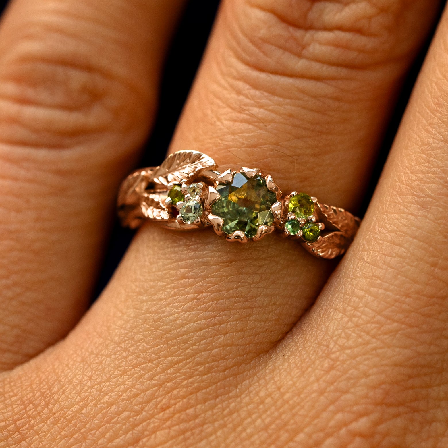 Close up view of a model's fingers wearing a 14k rose gold Green Sapphire Leaves and Vines Ring