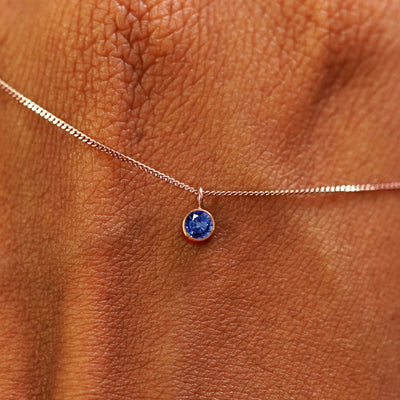 Close up view of a 14k rose gold Sapphire Necklace draped across the back of a model's hand