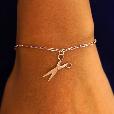 Close up view of a model's wrist wearing a rose gold Scissors Charm on a Butch Chain Bracelet