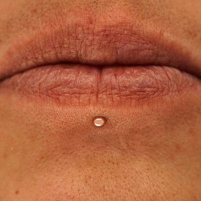 Close up view of a model's mouth wearing a 14k rose gold Small Ball Flatback as a labret piercing