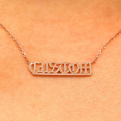 Close up view of a model's neck wearing a Small Custom Nameplate necklace that reads the word Custom