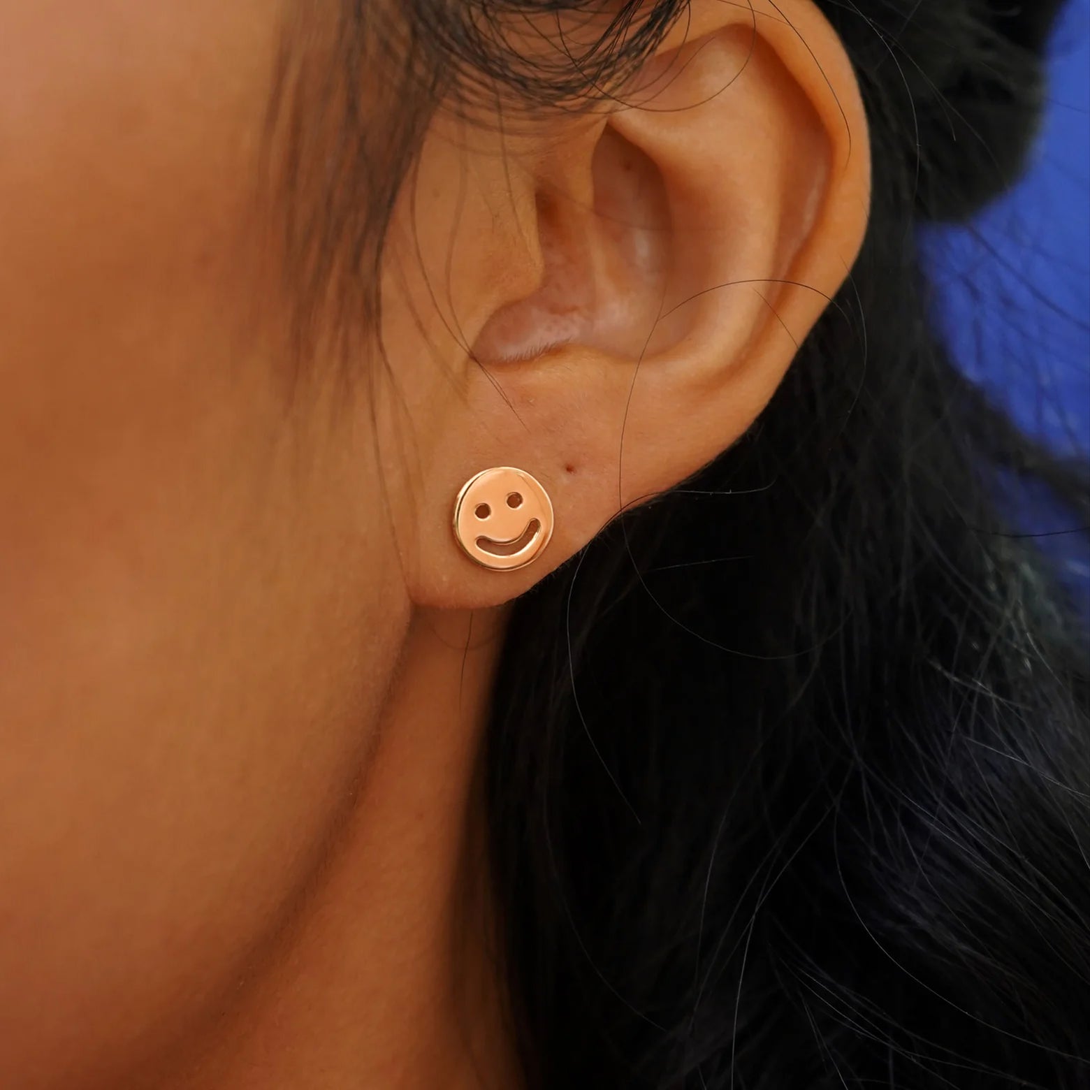 Close up view of a model's ear wearing a rose gold Smiley Face Earring