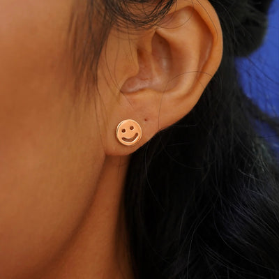 Close up view of a model's ear wearing a rose gold Smiley Face Earring