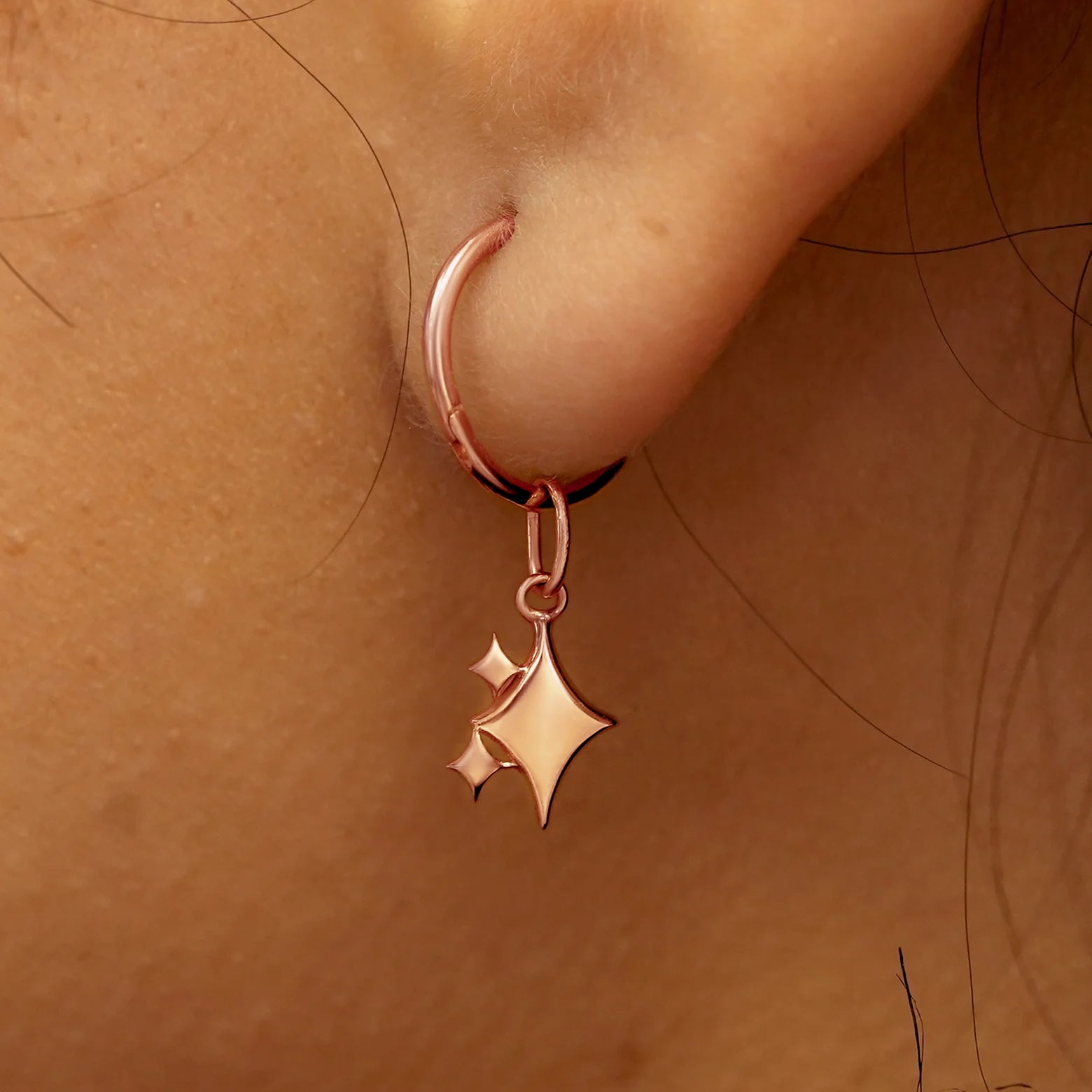 Close up view of a model's ear wearing a rose gold Sparkly Emoji Charm on a Small Seamless Huggie Hoop