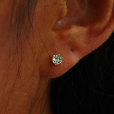 Close up view of a model's ear wearing a rose gold 4mm Montana Teal Sapphire Earring