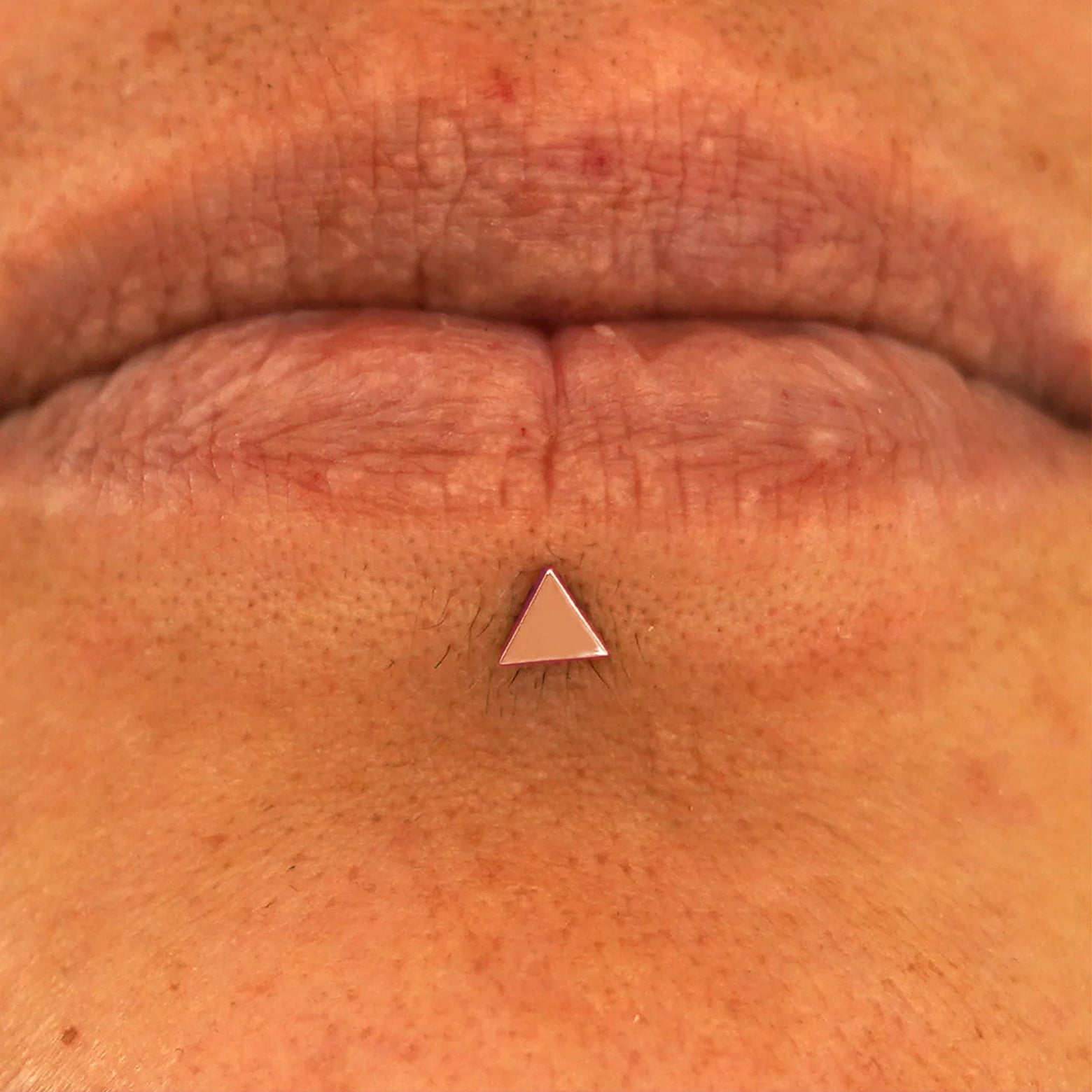 Close up view of a model's lips wearing a 14k rose gold Triangle Flatback in a labret piercing