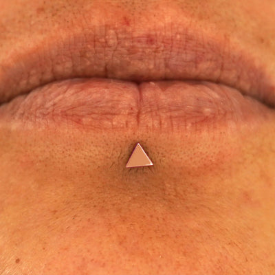 Close up view of a model's lips wearing a 14k rose gold Triangle Flatback in a labret piercing