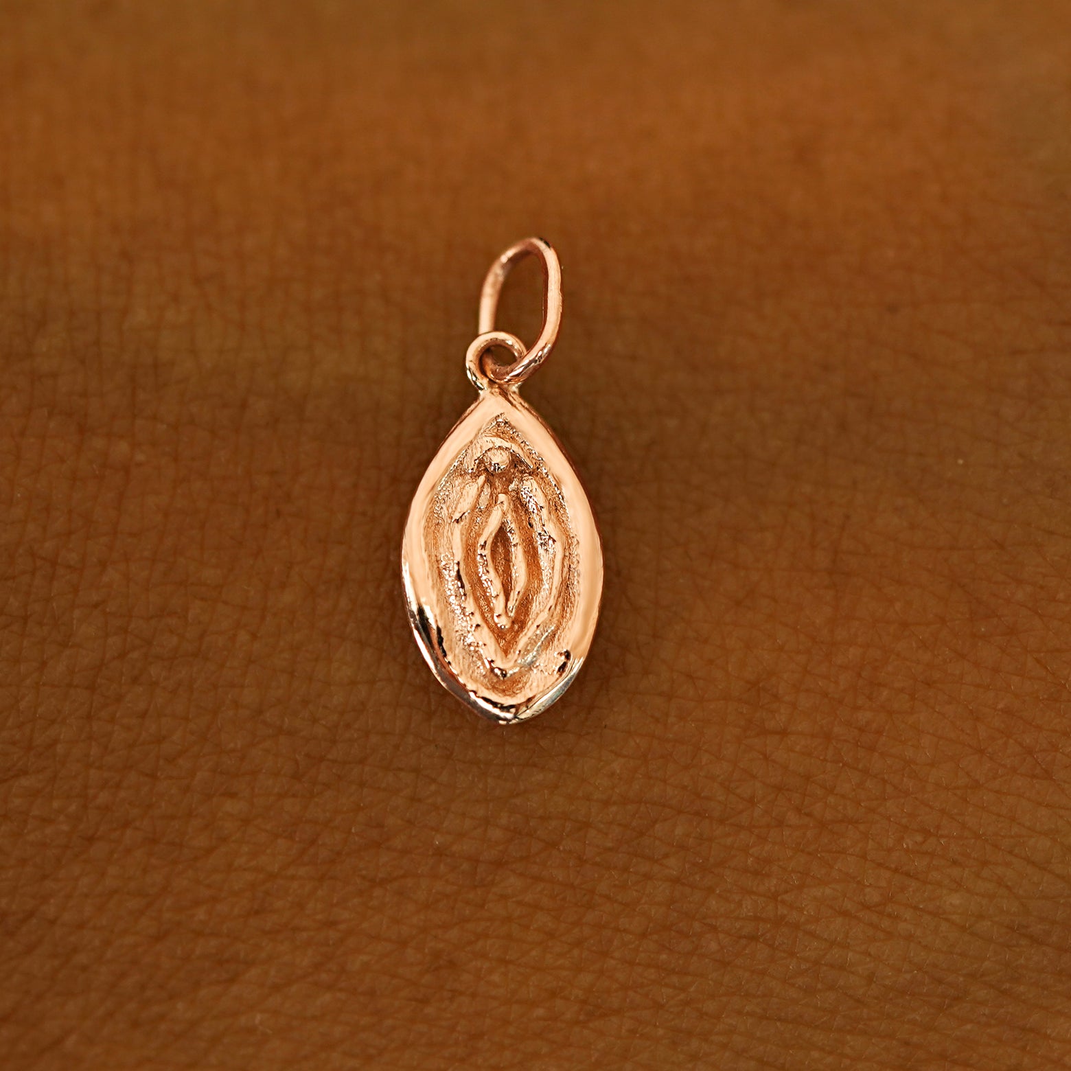 A solid 14k rose gold Vulva Charm resting on the back of a model's hand