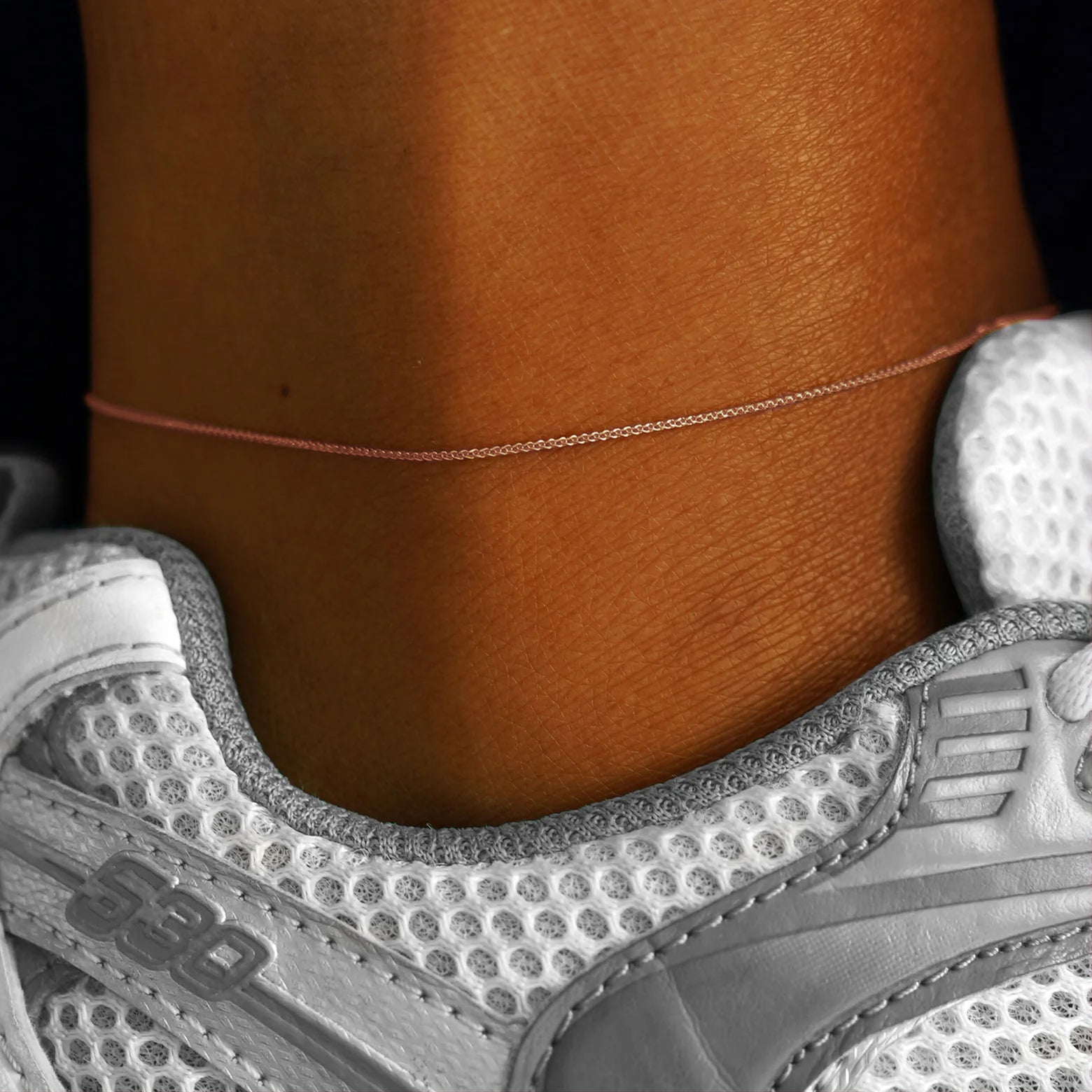 Close up view of a model's ankle wearing a solid 14k rose gold Wheat Chain