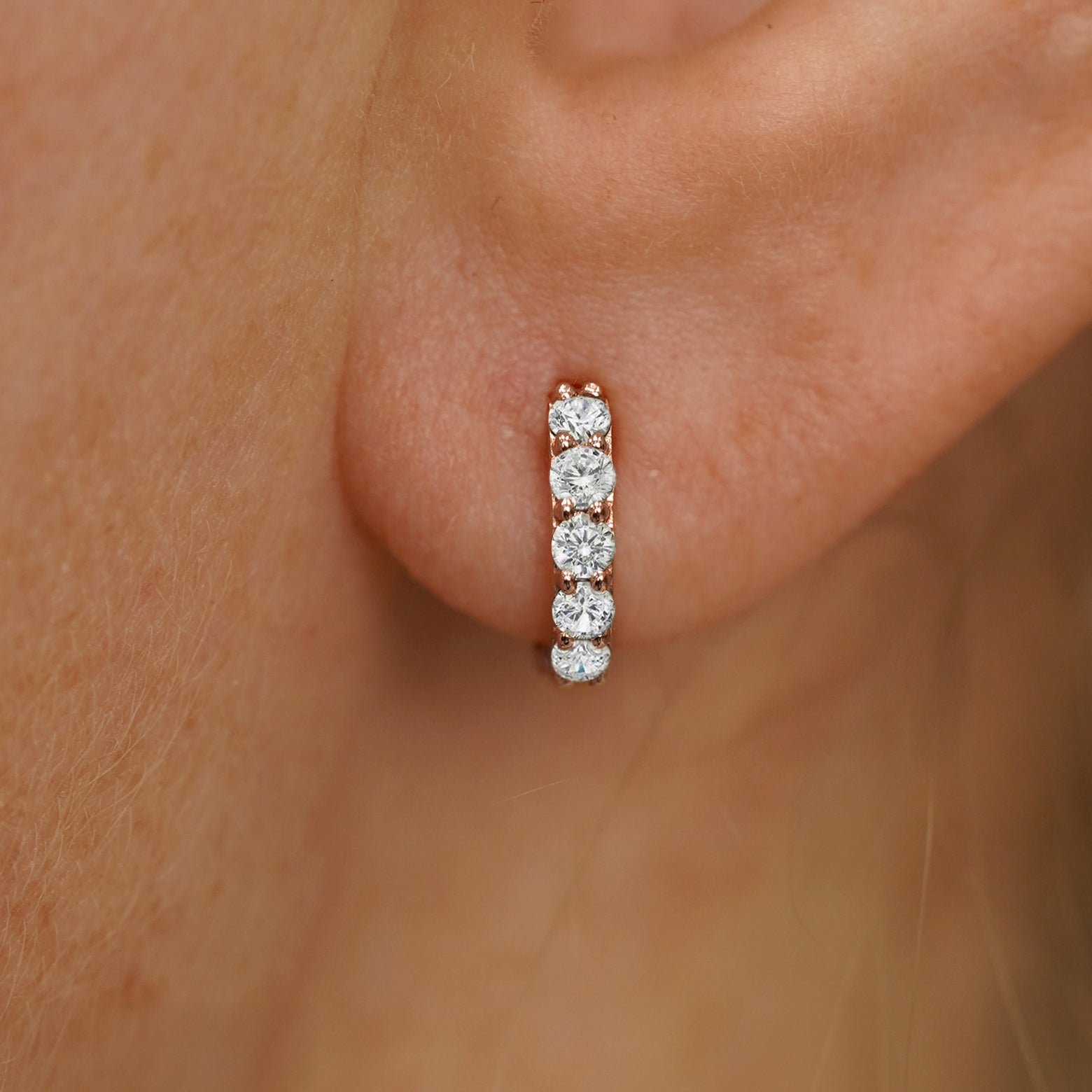 Close up view of a model's ear wearing a rose gold Mini Lab White Diamond Huggie Hoop