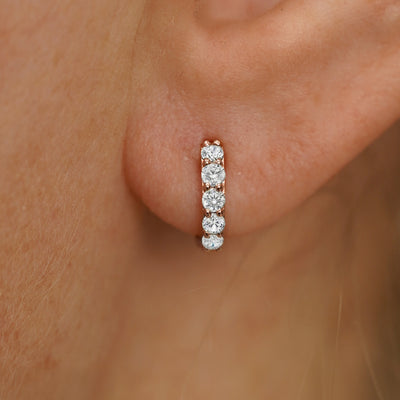 Close up view of a model's ear wearing a rose gold Mini Lab White Diamond Huggie Hoop