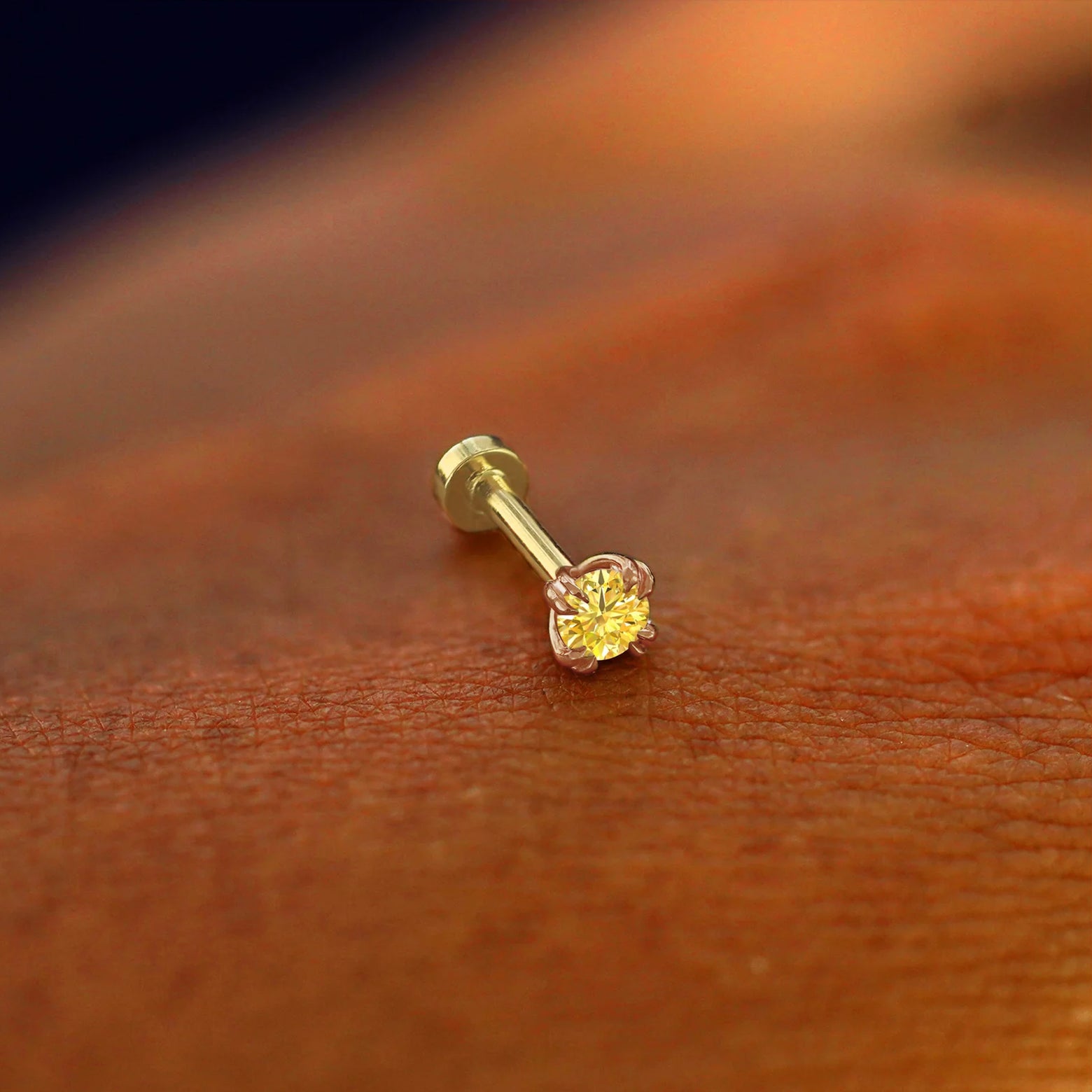 A solid 14k rose gold Yellow Diamond Piercing resting on the back of a model's hand
