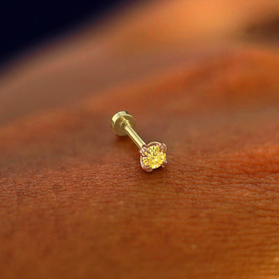 A solid 14k rose gold Yellow Diamond Piercing resting on the back of a model's hand
