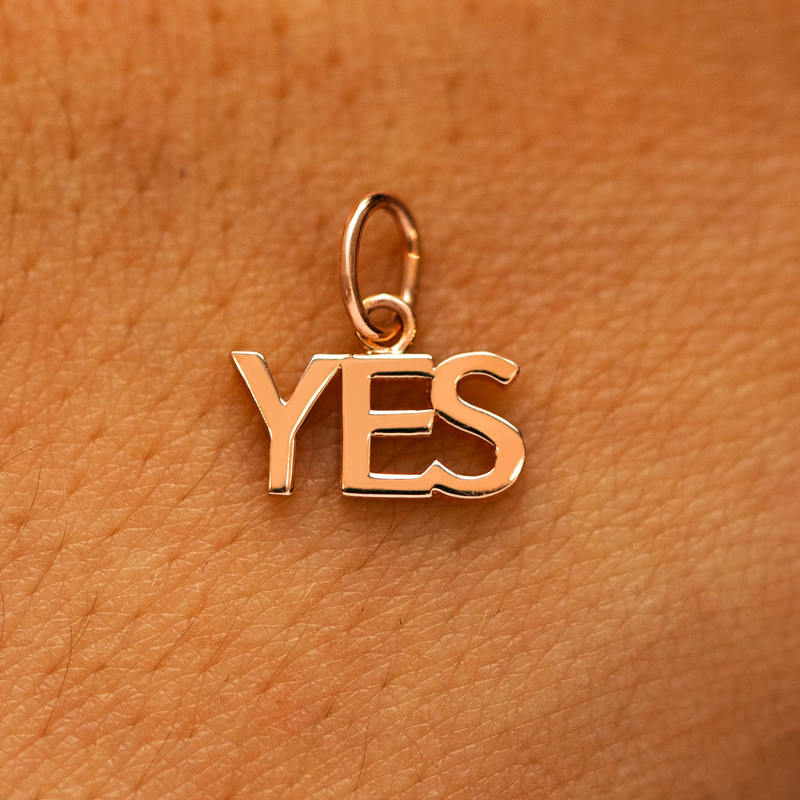 A solid 14k rose gold Yes Charm on the back of a models hand