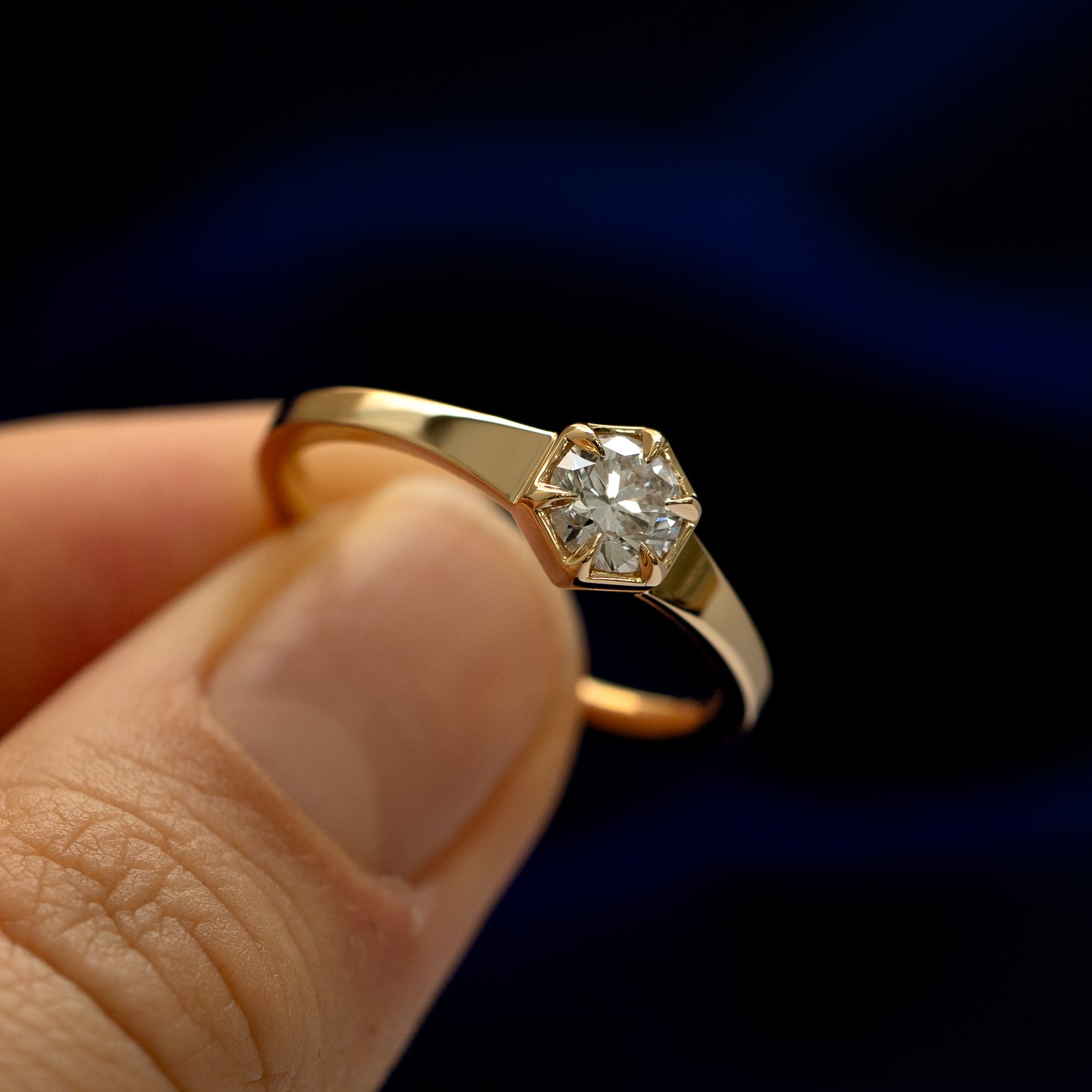 A model holding a round diamond hexagon signet ring tilted to show the claw setting around the stone