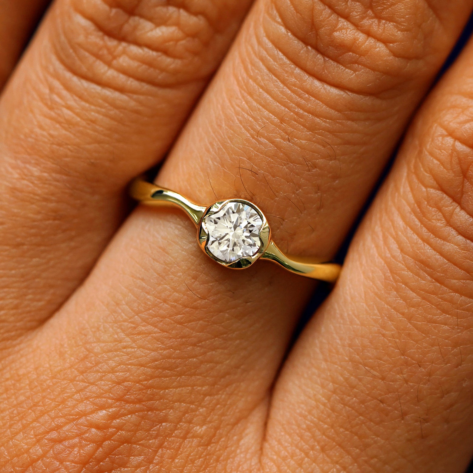 Close up view of a model's hand wearing a 14k yellow gold round lab clear diamond liquid ring