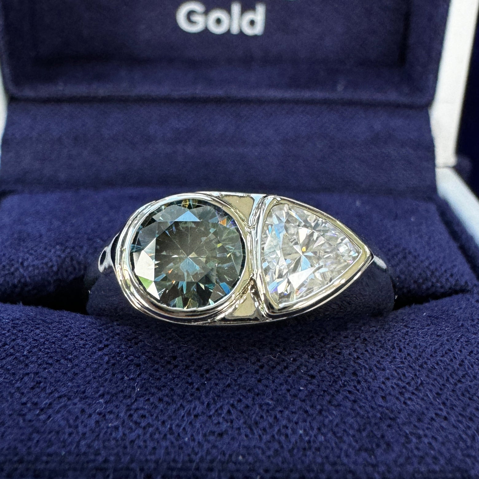 A photo of 14k Champagne Gold 6.5mm Round Gray Blue Moissanite with 6.5mm Trillion White Moissanite Custom Signet Ring in a blue ring box