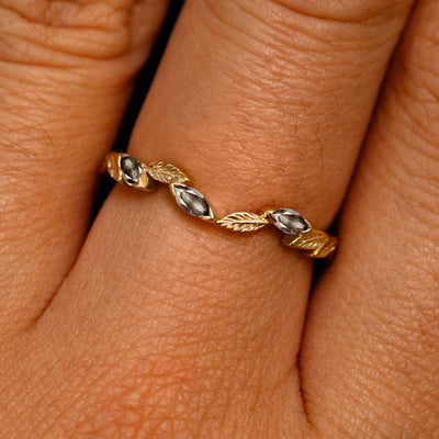 Close up view of a model's fingers wearing a 14k yellow gold Chevron Leaves and Marquise Salt and pepper Diamonds Band