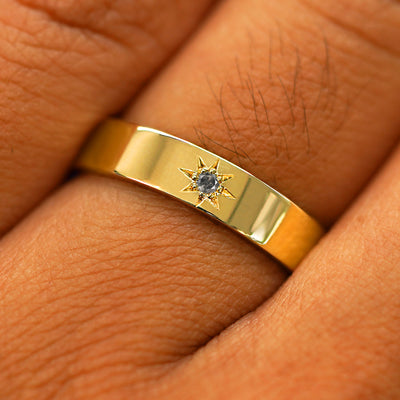 Close up view of a model's hand wearing a solid yellow gold Engraved Star Salt and Pepper Diamond Band
