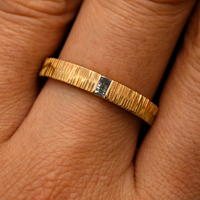 Close up view of a model's fingers wearing a 14k yellow gold Baguette Salt and Pepper Diamond Wood Band