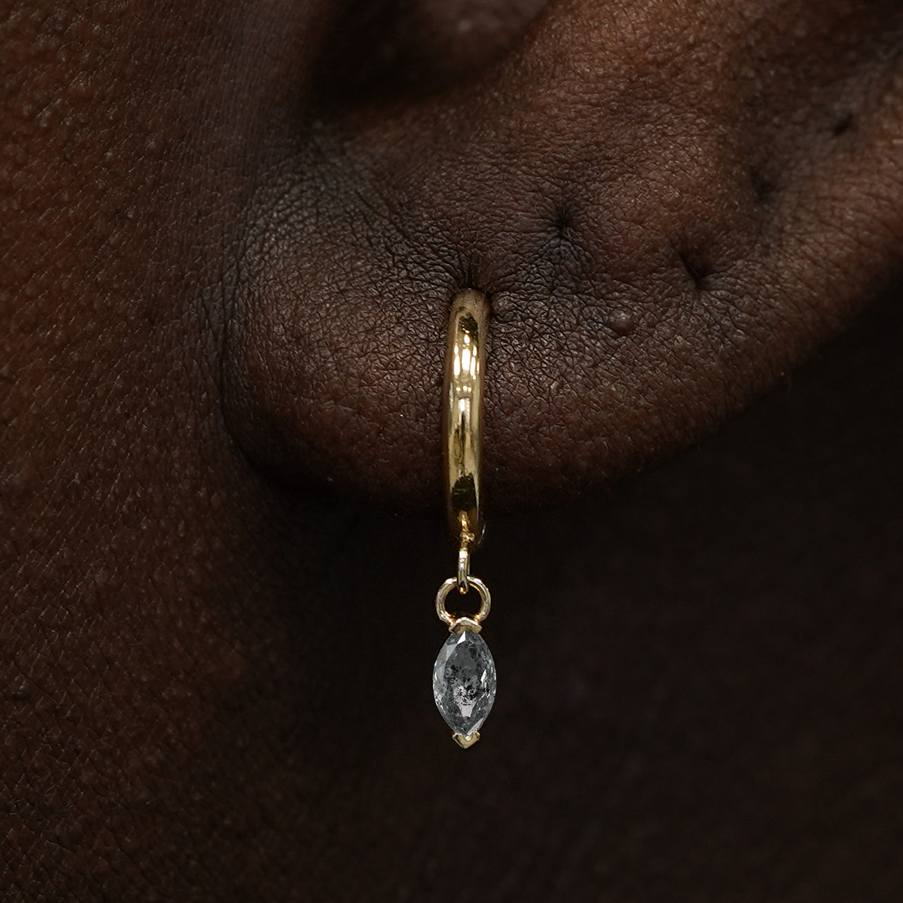 Close up view of a model's ear wearing a yellow gold Marquise Salt and Pepper Diamond Dangle Huggie Hoop