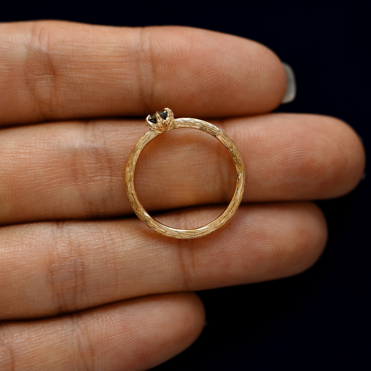 A yellow gold Montana Teal Sapphire Waved Branch Ring in a model's hand showing the thickness of the band