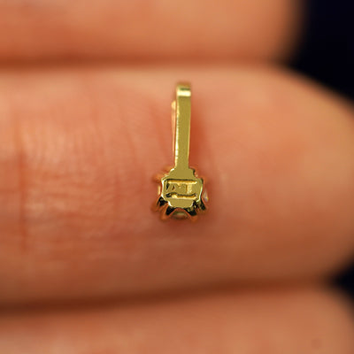 A solid gold Sapphire Charm for chain facedown on a model's fingertip to show the solid back of the charm