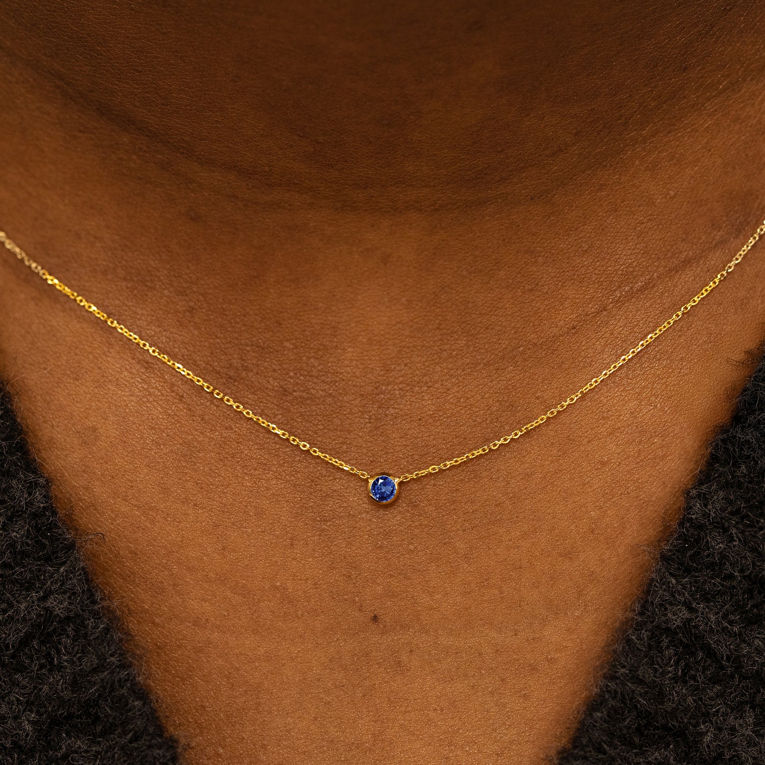 Close up view of a model neck wearing a 14k yellow gold Bezel set Sapphire gemstone necklace 