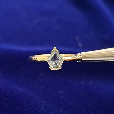 a custom-cut modified kite shape light green sapphire that is half-bezeled-set on a thin curvy band