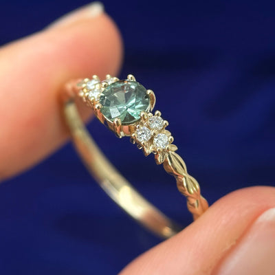 A model holding a 14k Yellow Gold Prongs-set 5mm Green Sapphire with 6pc white lab diamonds on Custom Leaves Band