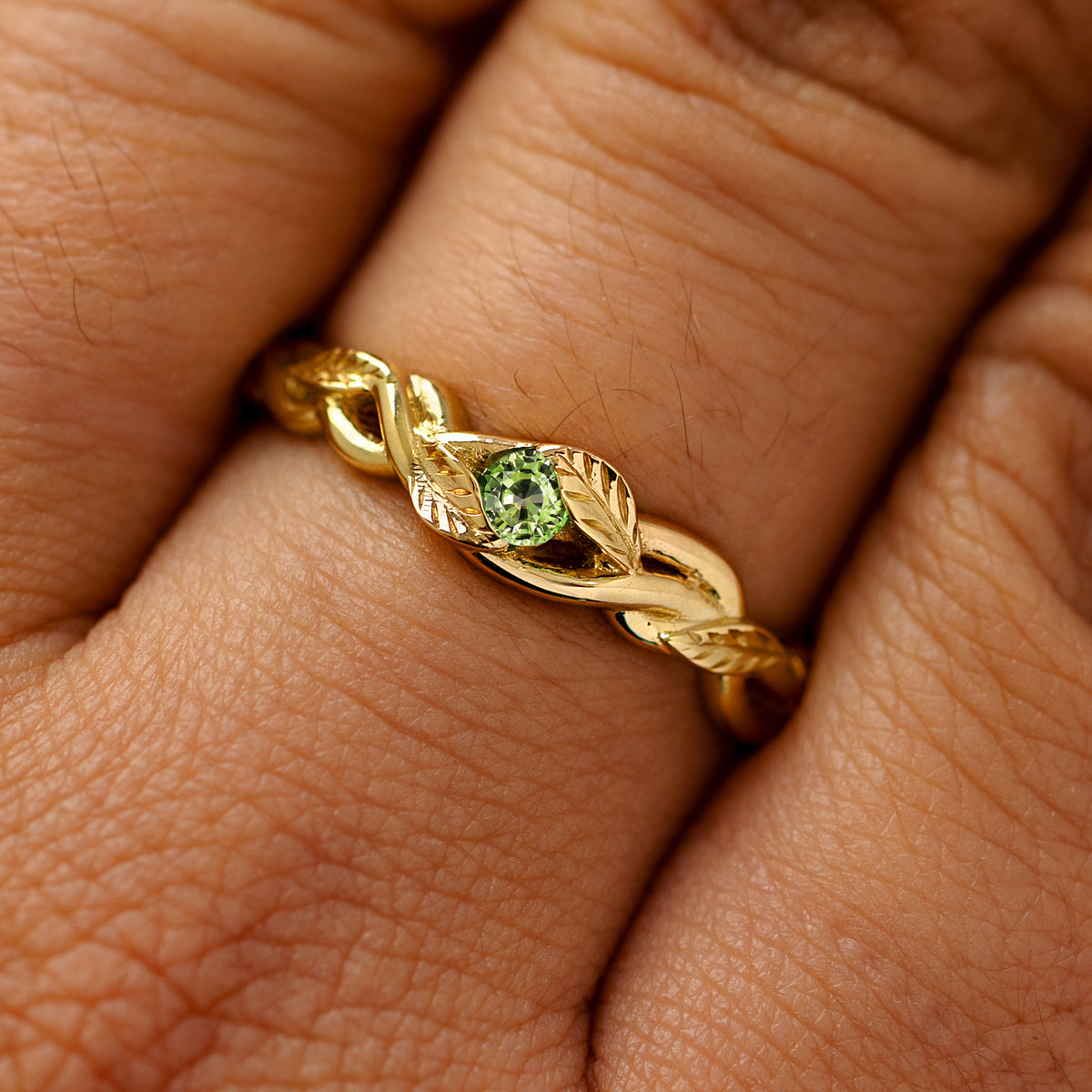 A solid 14k yellow gold teal sapphire leaves and vines ring on a model's finger
