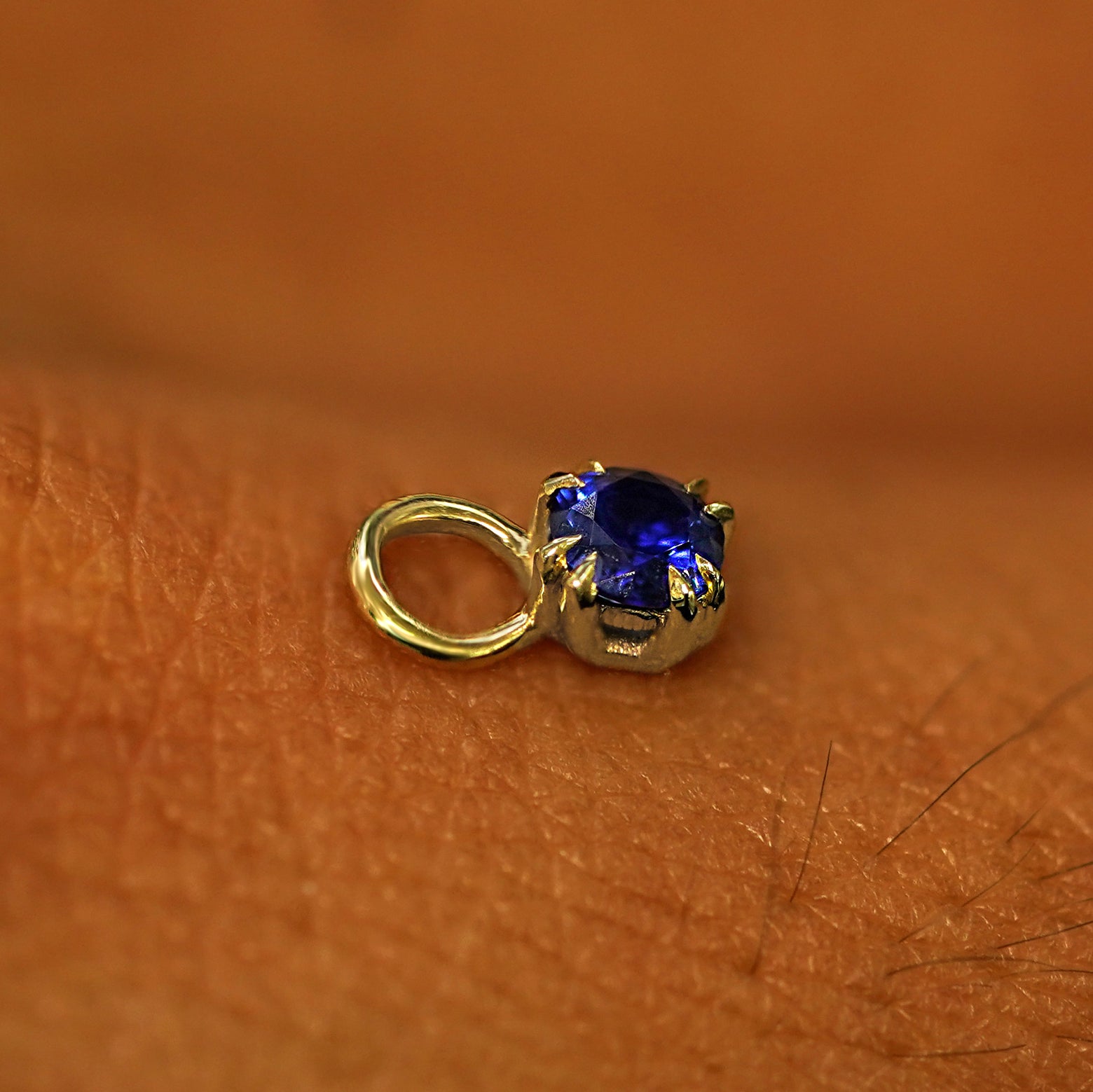 A solid yellow gold Sapphire Charm for earring resting on the back of a model's hand
