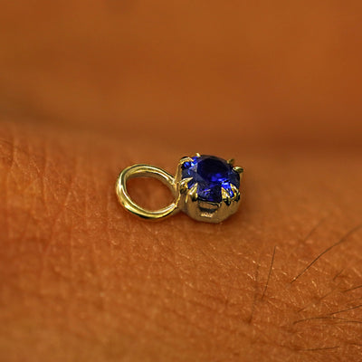 A solid yellow gold Sapphire Charm for earring resting on the back of a model's hand