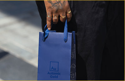 A customer wearing Automic Gold rings hold an Automic Gold branded blue shopping bag