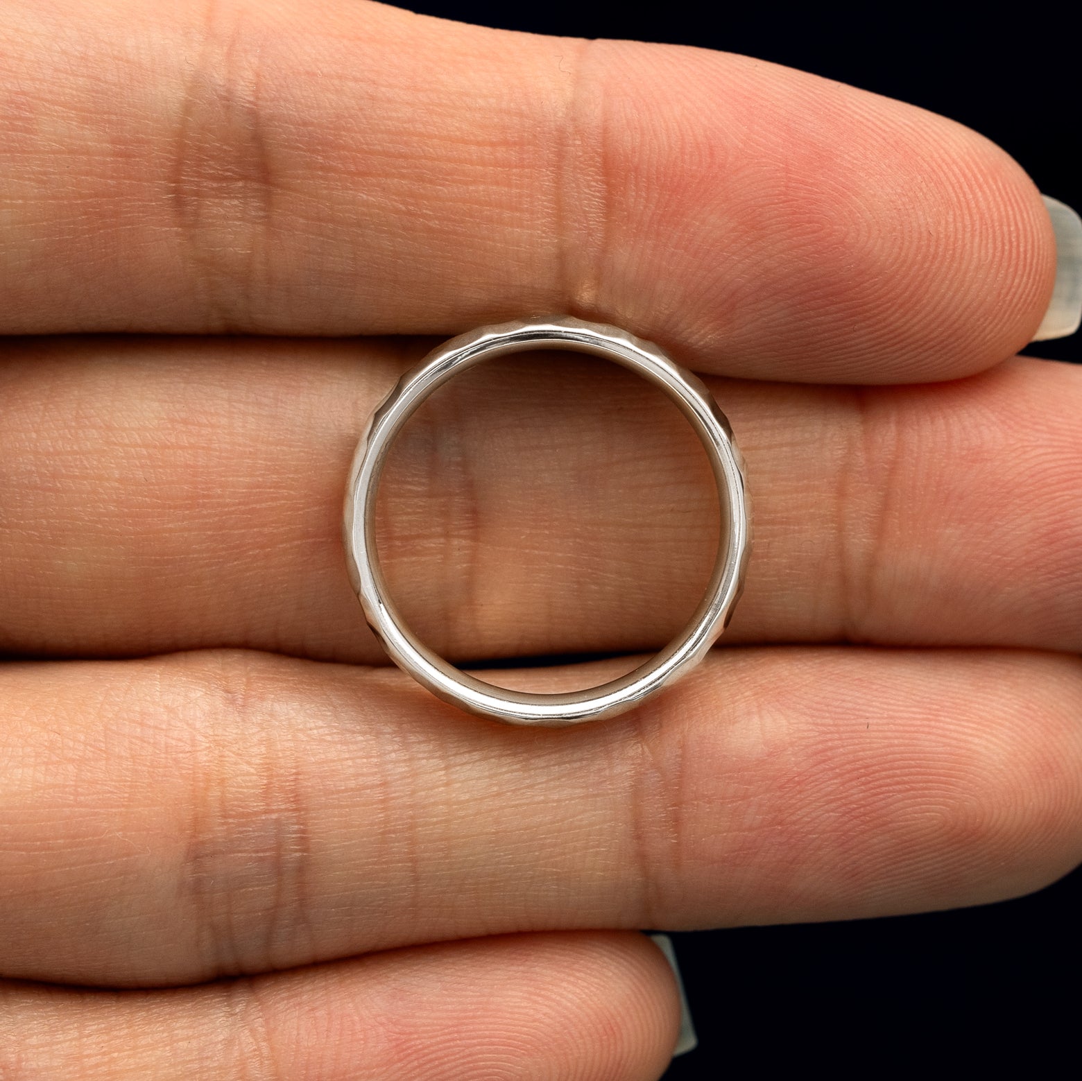A Silver Curvy Hammered Band resting on a model's fingers to show the thickness of the band