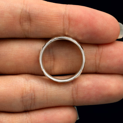 A Silver Curvy Hammered Band resting on a model's fingers to show the thickness of the band