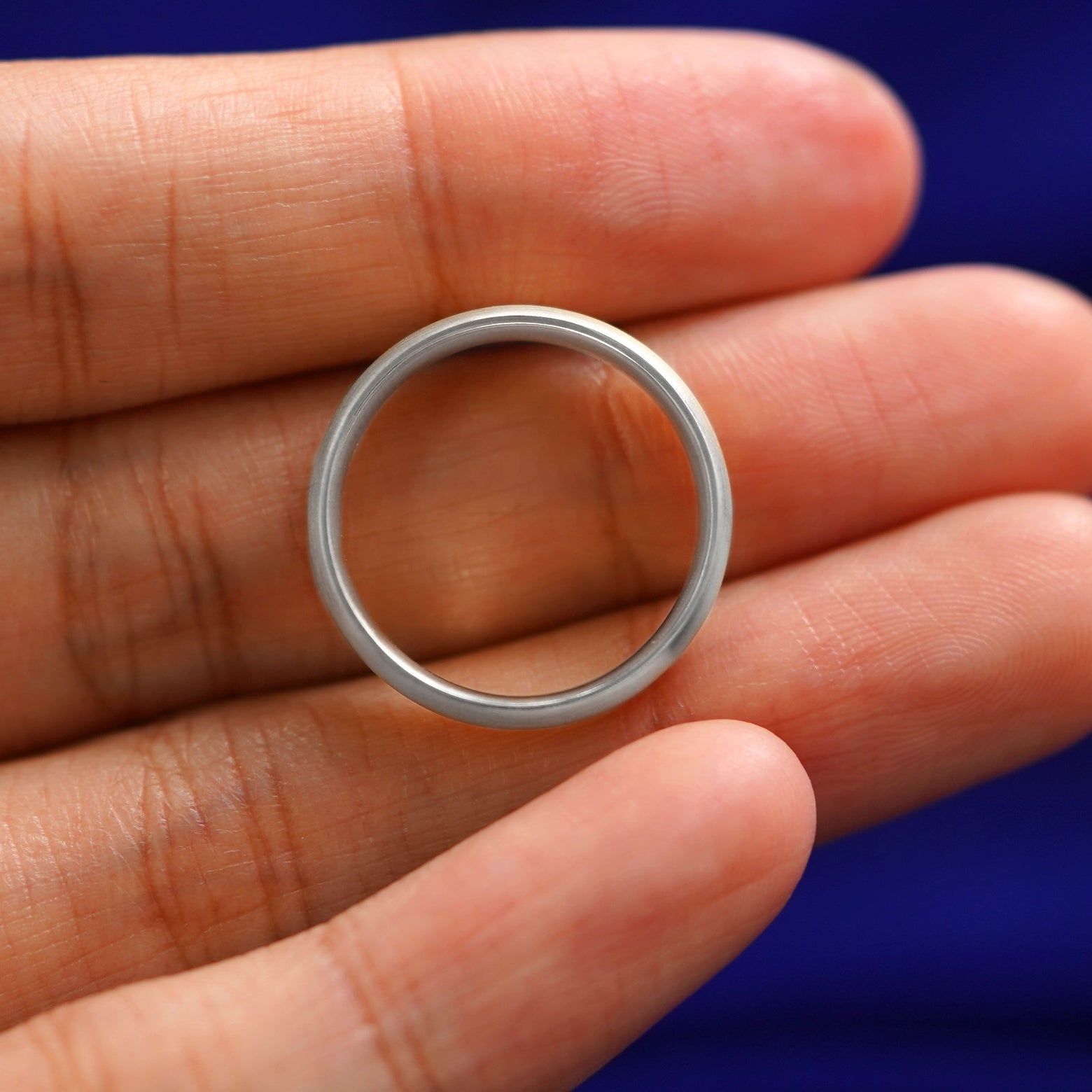 A Silver Curvy Matte Band resting on a model's fingers to show the thickness of the band