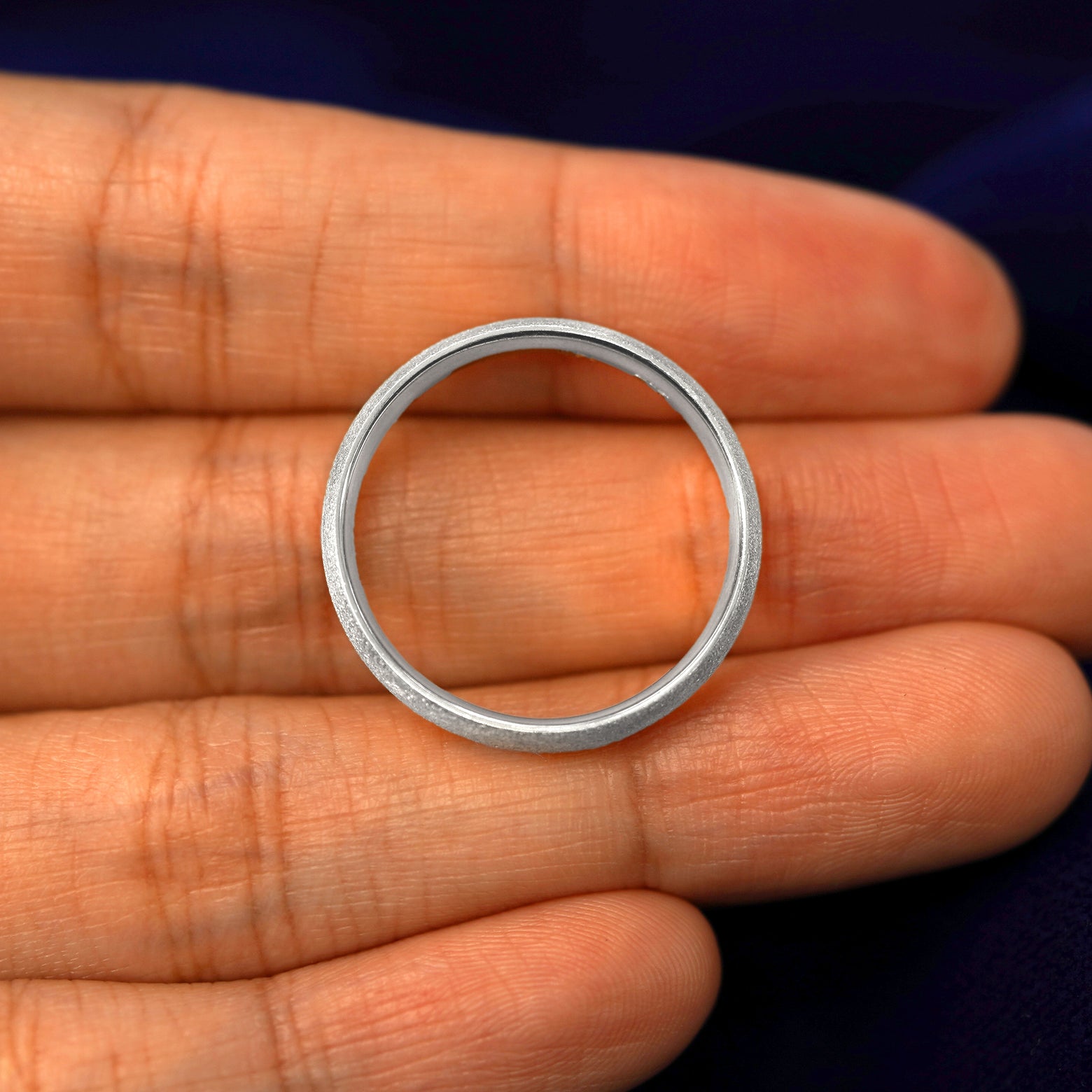 A silver Curvy Stardust Band in a model's hand showing the thickness of the band