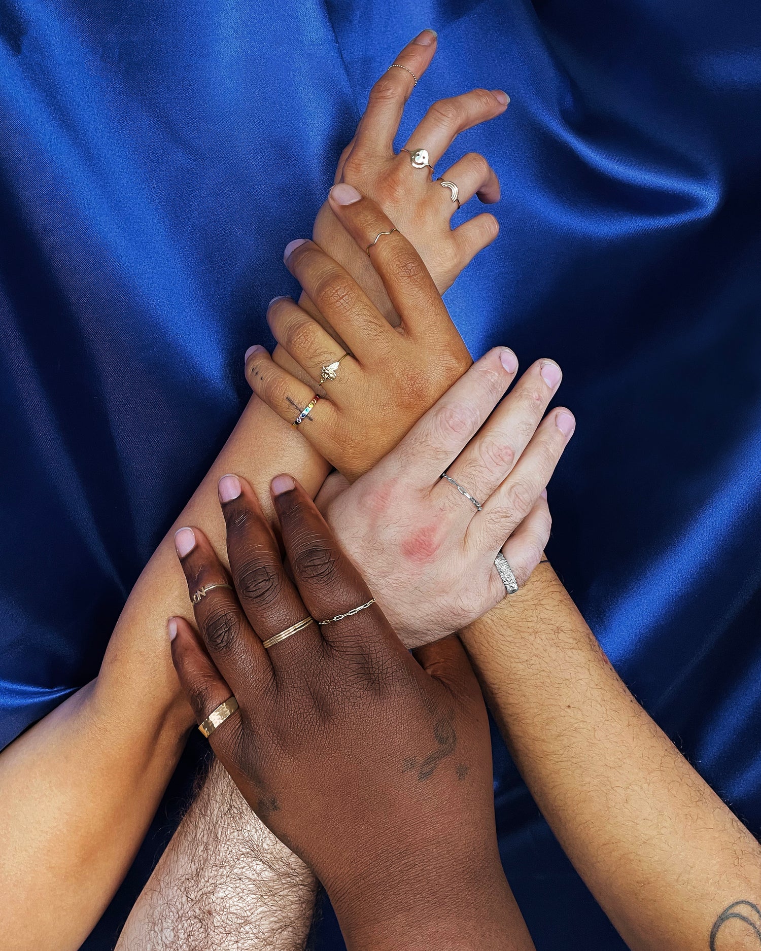 Four hands of four different model's holding each others wrists upwards in a criss cross pattern all wearing solid gold rings
