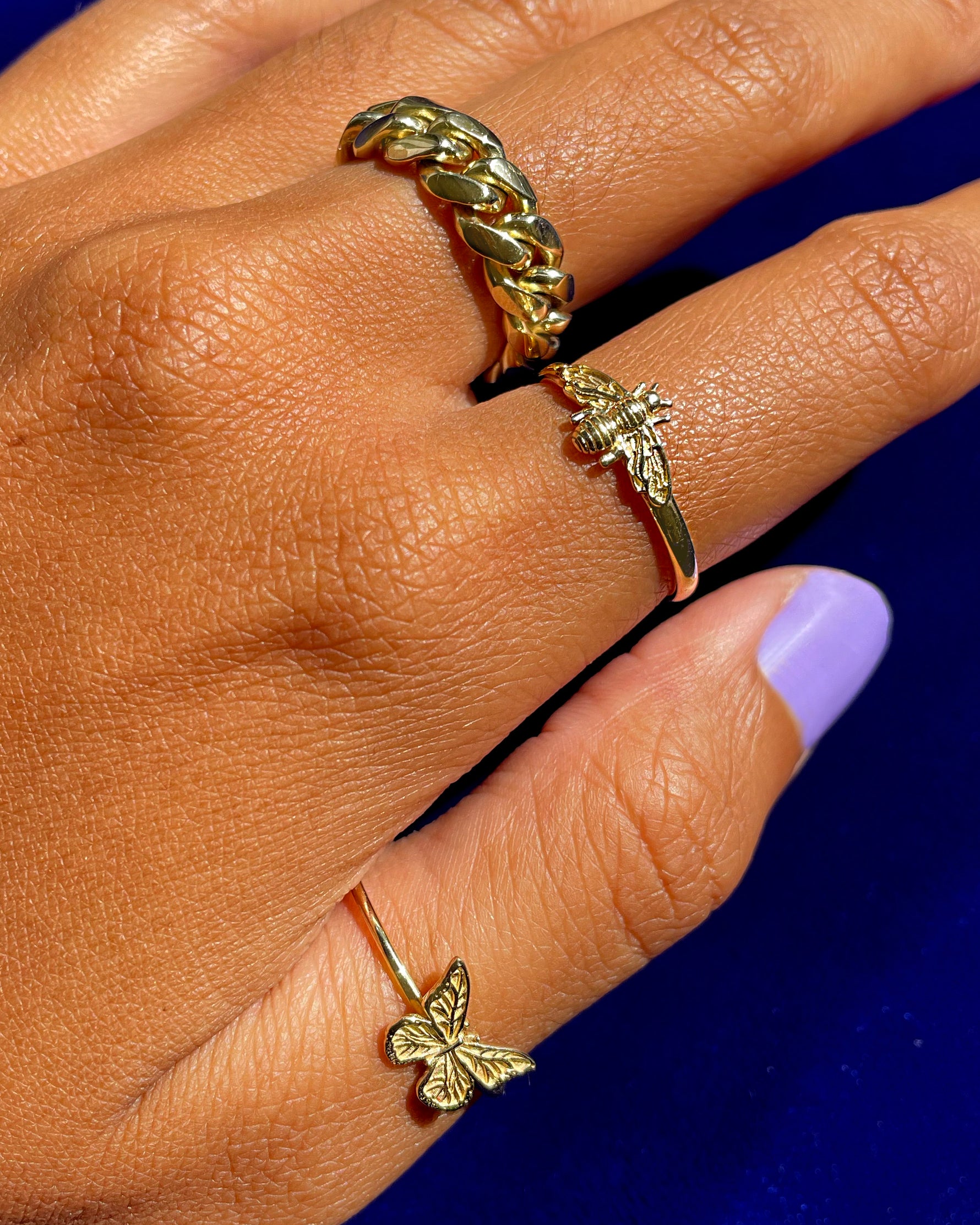 A model's with purple nails wearing a Miami Ring, a Curvy Bee Ring, and a Butterfly ring all in yellow gold