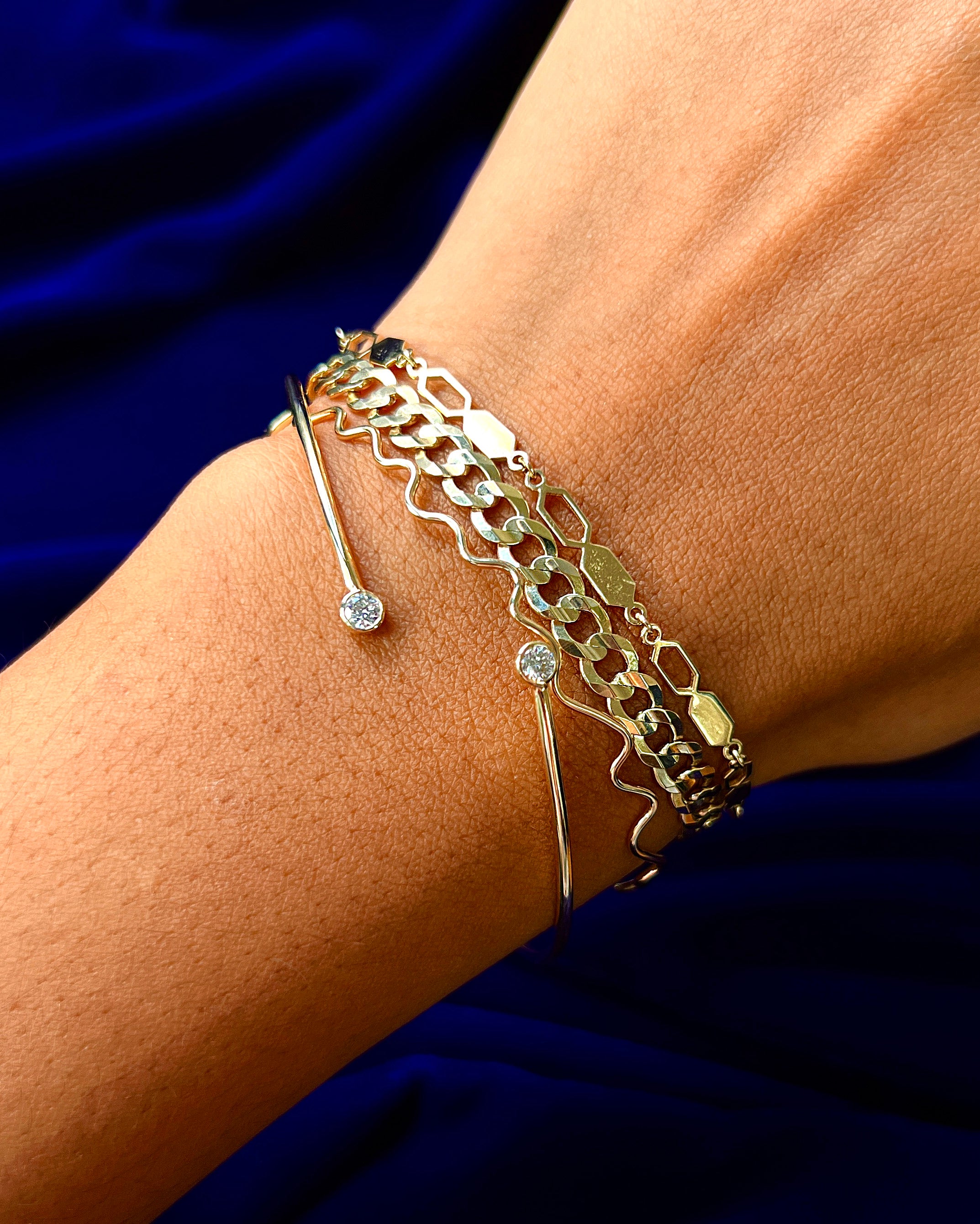 Close up view of a model's hand wearing a Line Bangle, a Bound Together, and a Custom Bracelet: Inset of a Curb Bracelet