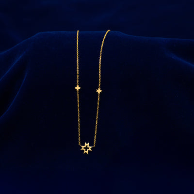A solid gold 8 pointed star necklace draped across a dark blue cloth