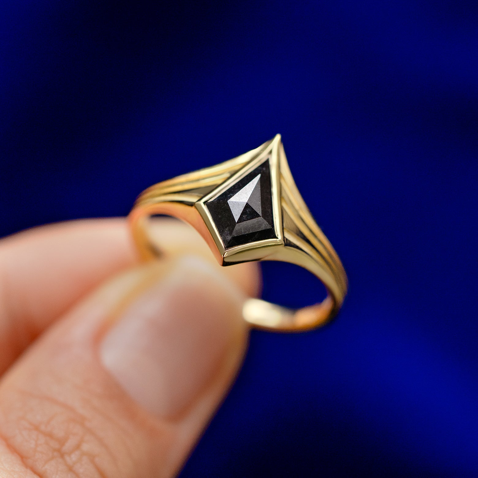A model holding a solid gold Journey Ring between two fingers to show the faceted kite-shaped black diamond