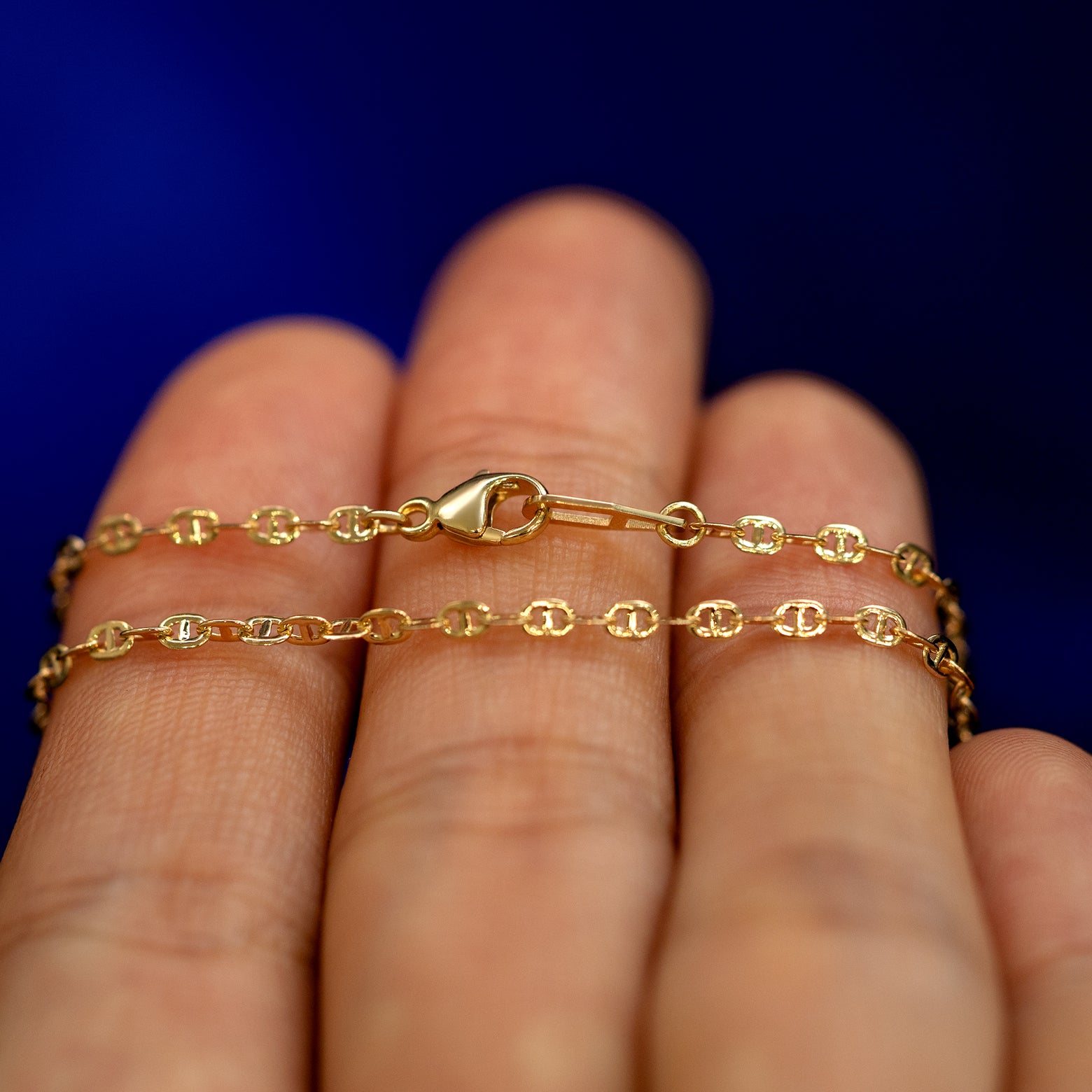 A yellow gold Flat Mariner Chain Bracelet wrapped around a model's fingers to show the chain and the lobster claw clasp
